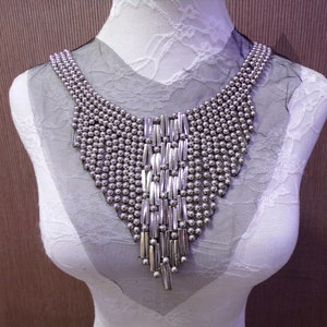 May include: A silver beaded and metal chain necklace with a V-shaped design. The necklace is displayed on a white mannequin.