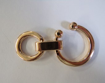Puede incluir: Cierre de metal dorado con dos bucles circulares. El cierre está diseñado para conectar dos piezas de material.