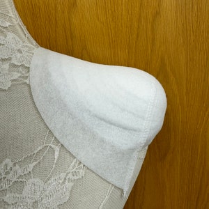 Puede incluir: Una silla de encaje blanco con un reposabrazos acolchado blanco. La silla está contra un fondo de panel de madera.