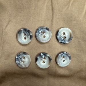 Puede incluir: Seis botones marmoleados blancos y negros con dos agujeros cada uno.