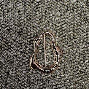 May include: A gold-coloured, abstract, irregular-shaped belt buckle.