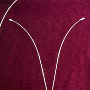 May include: Two silver metal headbands with white plastic tips. The headbands are curved and form a V shape.