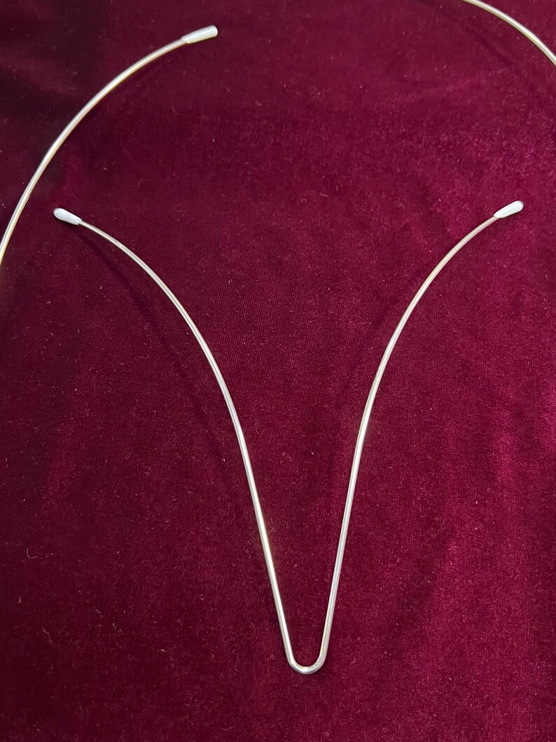 May include: Two silver metal headbands with white plastic tips. The headbands are curved and form a V shape.