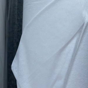 May include: A close-up of a white fabric roll with a textured surface. The fabric is folded and has a slight sheen.