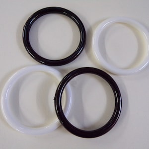 May include: Four plastic bangles, two white and two dark brown, arranged on a white surface.