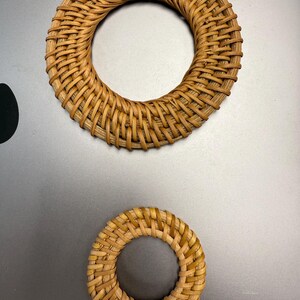 May include: Two circular woven rattan placemats, one large and one small, on a grey surface. The placemats are made of light brown woven rattan and have a hole in the centre.