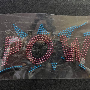 Puede incluir: Primer plano de una hoja transparente con la palabra "BOY" escrita en pedrería rosa y azul.