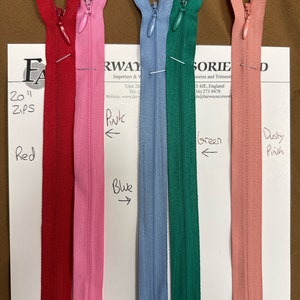 Könnte beinhalten: Fünf Reißverschlussbänder in verschiedenen Farben: Rot, Rosa, Blau, Grün und Altrosa. Die Reißverschlussbänder liegen auf einer weißen Oberfläche mit Textbeschriftungen für jede Farbe.