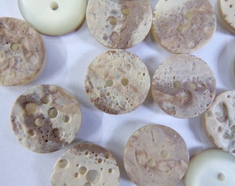 May include: A collection of round, brown and white marbled buttons with two holes each. The buttons have a textured surface and a speckled appearance.