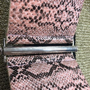 May include: A pink and black snakeskin belt with a silver buckle. The belt is made from soft, supple leather and has a subtle sheen.
