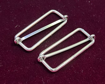 May include: Two silver metal slider buckles, often used for adjusting straps on clothing or bags.