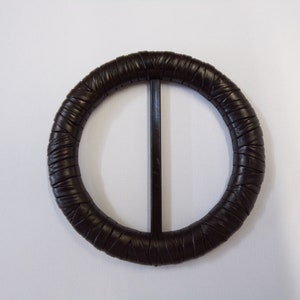 Könnte beinhalten: Eine schwarze Ledergürtelschnalle mit rundem, geflochtenem Design.