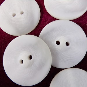May include: A collection of six white, round, two-hole buttons. The buttons are made of a smooth, shiny material and have a slightly raised center.