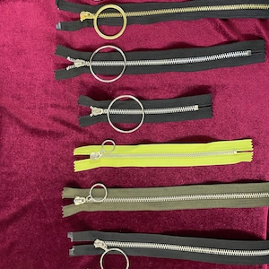 Peut inclure: Un ensemble de sept tirettes de fermeture éclair différentes avec des anneaux métalliques. Les fermetures éclair sont de différentes couleurs, notamment noir, vert et jaune.