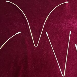 May include: Three bent metal rods with white cotton tips on each end. The rods are arranged in a V shape, with the tips pointing upwards.