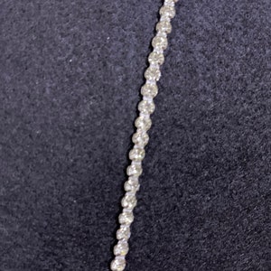 Könnte beinhalten: Nahaufnahme einer silbernen Kette mit kleinen, runden, klaren Strasssteinen. Die Kette liegt auf einem schwarzen Hintergrund.