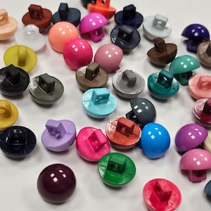 Puede incluir: Surtido de botones de plástico en forma de cúpula de colores con un vástago cuadrado. Los botones son de varios colores, incluidos rojo, azul, verde, amarillo, morado, rosa, marrón, negro y blanco.