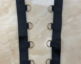 May include: Black ribbon with gold metal rings sewn along the edges. The ribbon is approximately 1 inch wide.
