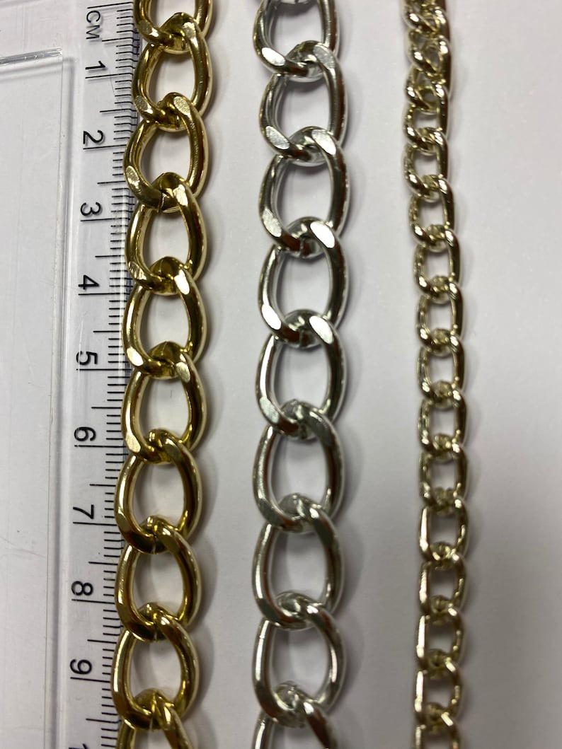 May include: Three chains of different styles and colors. The chain on the left is gold and has large oval links. The chain in the middle is silver and has smaller oval links. The chain on the right is gold and has small square links.