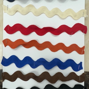 May include: A collection of eight wavy fabric trims in various colours, including navy blue, cream, red, orange, blue, brown, and black.