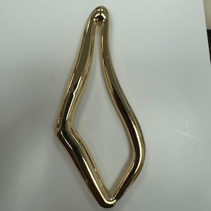 May include: A gold-coloured metal ring with a unique, abstract shape. The ring is smooth and shiny.