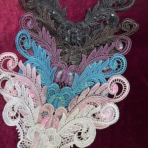 Puede incluir: Un conjunto de cinco aplicaciones de encaje en varios colores, incluyendo blanco, rosa, azul, morado y negro. Cada aplicación presenta un delicado diseño floral con detalles intrincados y lentejuelas brillantes.