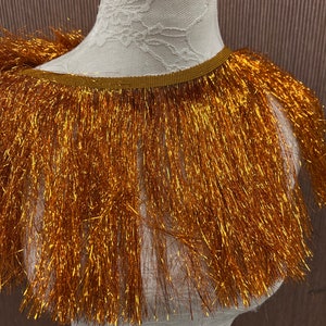May include: Gold metallic fringe trim with a brown backing. The fringe is approximately 2 inches long.