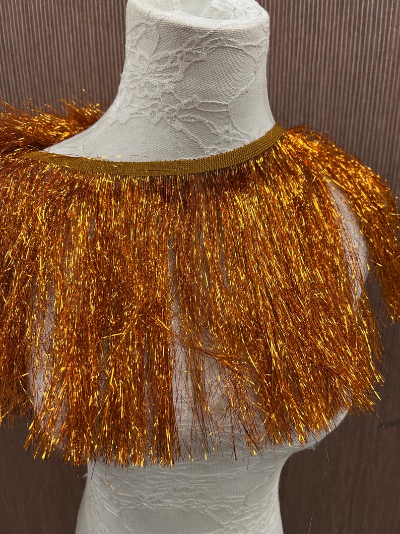 May include: Gold metallic fringe trim with a brown backing. The fringe is approximately 2 inches long.