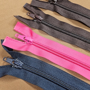 Può includere: Quattro chiusure a zip di diversi colori, tra cui nero, blu navy, marrone e rosa. Le cerniere sono disposte in fila su una superficie marrone.