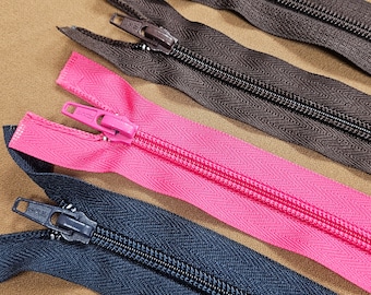 Könnte beinhalten: Vier verschiedene Reißverschlüsse in verschiedenen Farben, darunter Schwarz, Dunkelblau, Braun und Pink. Die Reißverschlüsse liegen in einer Reihe auf einer braunen Oberfläche.