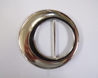 Puede incluir: Una hebilla de cinturón de metal plateado con forma ovalada redondeada y lisa, con una barra recta en el centro.