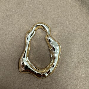 May include: A gold-colored, abstract, irregular shaped ring. The ring is smooth and shiny.