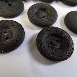 May include: A close-up of black buttons with a textured surface. The buttons have two holes each.