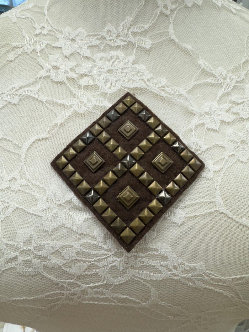 May include: A brown diamond-shaped patch with a pattern of silver and gold pyramid-shaped studs.