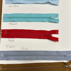 May include: Five different colours of 5 inch zippers. The colours are light blue, aqua, red, blue, and brown.