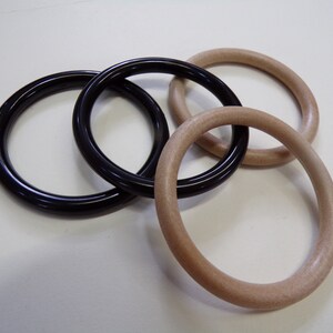 Puede incluir: Cuatro anillos, dos negros y dos marrón claro, están apilados sobre una superficie blanca. Los anillos tienen todos aproximadamente 7,5 cm de diámetro.