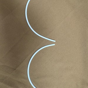 May include: Two white plastic bra underwire supports. The supports are curved and are on a brown fabric background.