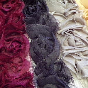 May include: Four strips of fabric with ruffled edges, each in a different colour: burgundy, black, grey, and beige. The fabric is arranged vertically, with the burgundy strip on the left and the beige strip on the right.