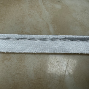 May include: A close-up of a silver fabric strip with a straight stitch running along the centre.
