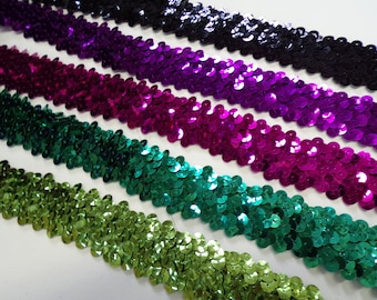 Puede incluir: Primer plano de cinco filas de ribete de lentejuelas en negro, morado, magenta, verde azulado y verde. El ribete está hecho de pequeñas lentejuelas redondas que están cosidas juntas en una línea continua.