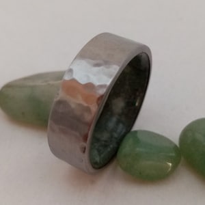 May include: A silver hammered metal ring with a smooth, polished interior. The ring is surrounded by five small, light green stones.