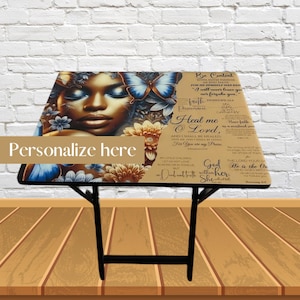 May include: A folding table with a colorful design featuring a woman's face, butterflies, and flowers. The table top has a quote from the Bible: "Be Content for He Himself Has Said, 'I will never leave you nor forsake you.'"