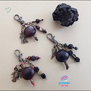 Peut inclure: Deux porte-clés avec des gousses de graines brunes, des breloques en métal et des perles. Un porte-clés a un charme de chat et l'autre un charme d'aile d'ange. Les deux porte-clés ont des perles de roche volcanique noire.