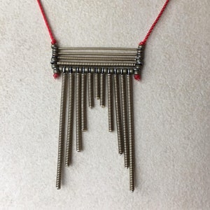 May include: A gold-toned necklace with a rectangular pendant made of coiled wire and beads. The pendant has a fringe of coiled wire hanging from the bottom.