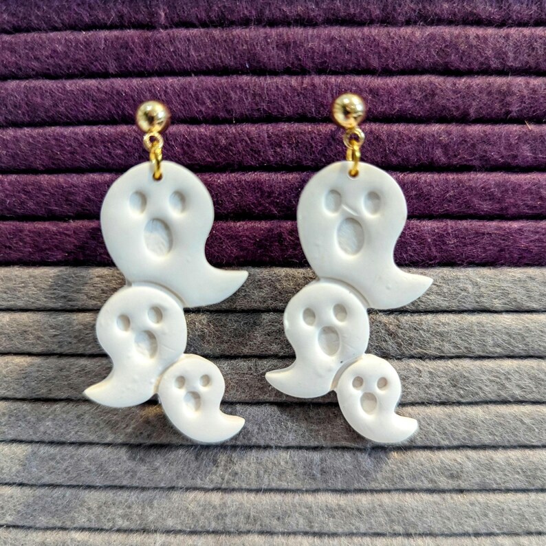 Pode incluir: Brincos de argila polim&eacute;rica em forma de fantasma branco com ganchos de ouro. Os brincos s&atilde;o feitos de tr&ecirc;s fantasmas, cada um com um rosto.