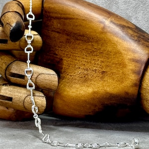 May include: Silver necklace with a chain made of linked horse stirrup charms.