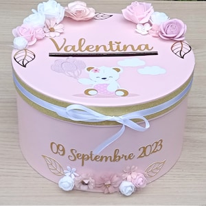 Peut inclure: Boîte ronde rose avec un ruban doré et un nœud blanc. La boîte est décorée de fleurs, de feuilles et d'un ours en peluche tenant un ballon. Le texte "Valentina" et "09 Septembre 2023" est écrit sur la boîte.