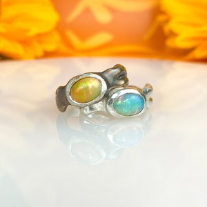 May include: Two silver rings with opal gemstones. The ring on the left has a yellow opal, and the ring on the right has a blue opal.