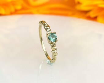 May include: A gold ring with a textured band and a small, round, light blue gemstone.