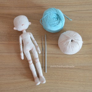 May include: A white crocheted doll with a light blue and a beige ball of yarn and two crochet hooks on a wooden surface. The text '@stitcheshandmade' is visible in the bottom right corner of the image.